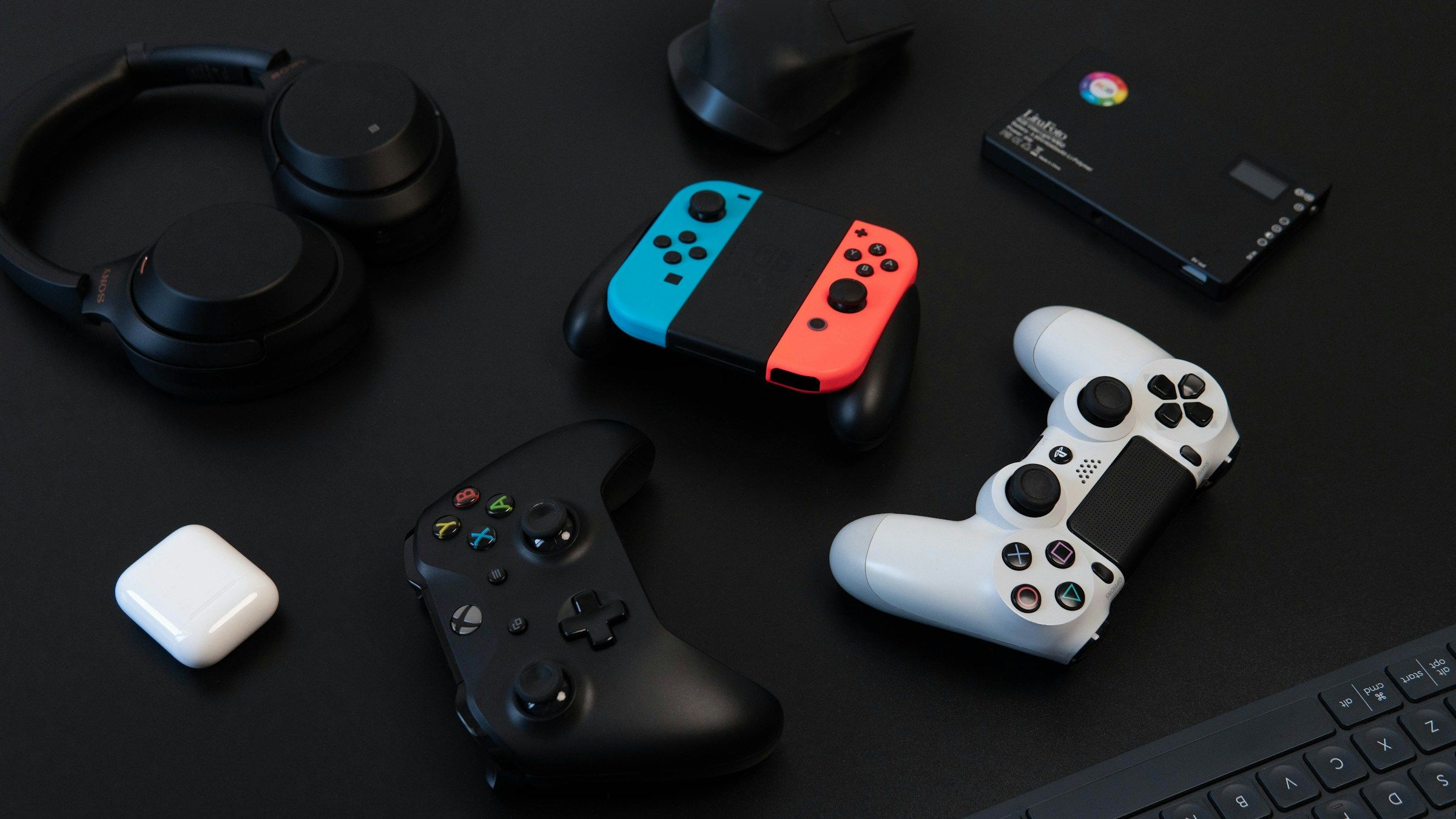 Nintendo Switch Joy-Con, Xbox and PlayStation controllers, and headphones on a dark desk